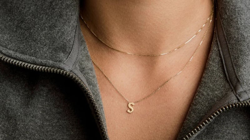 A person wearing two necklaces, one of which is the Mejuri | Letter Necklace.