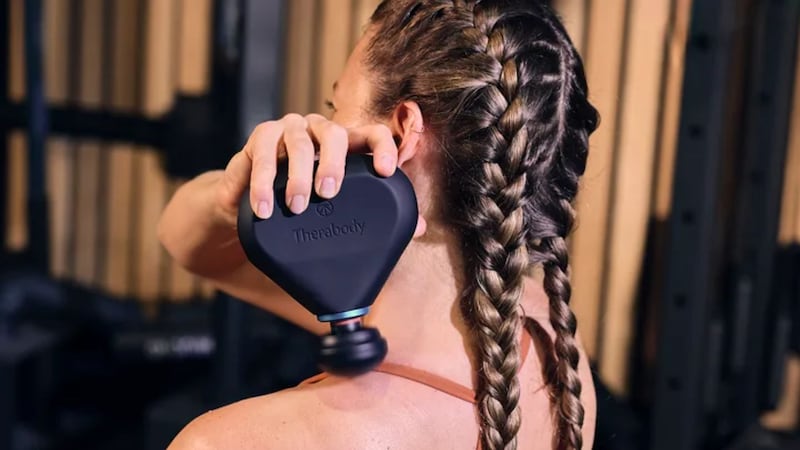 A person massaging their shoulder with the Theragun Mini Plus Massage Gun by Therabody.