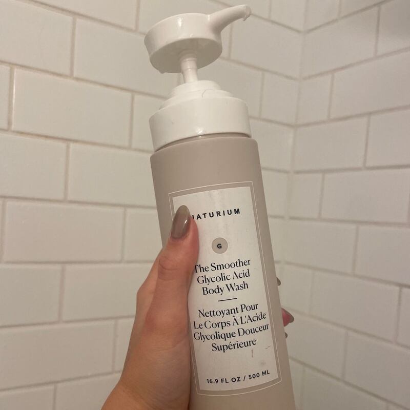 Alice holding a bottle of Naturium body wash in her shower.
