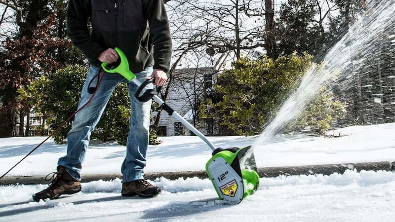 A person using an electric snow shovel on a driveway.