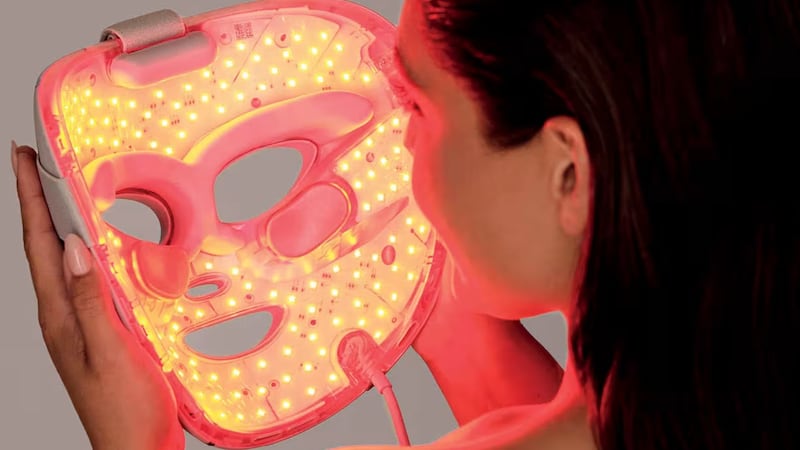 A person holding the lit-up Shark CryoGlow LED Face Mask in front of their face.