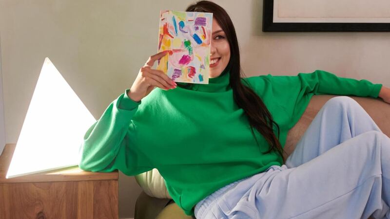 A person on a couch holding a journal next to a light therapy lamp.