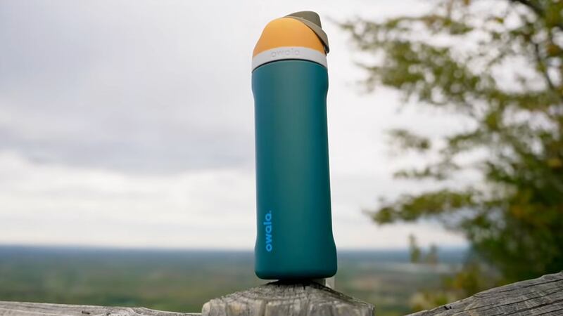 the owala bottle outside on a fence with a vast field in the background